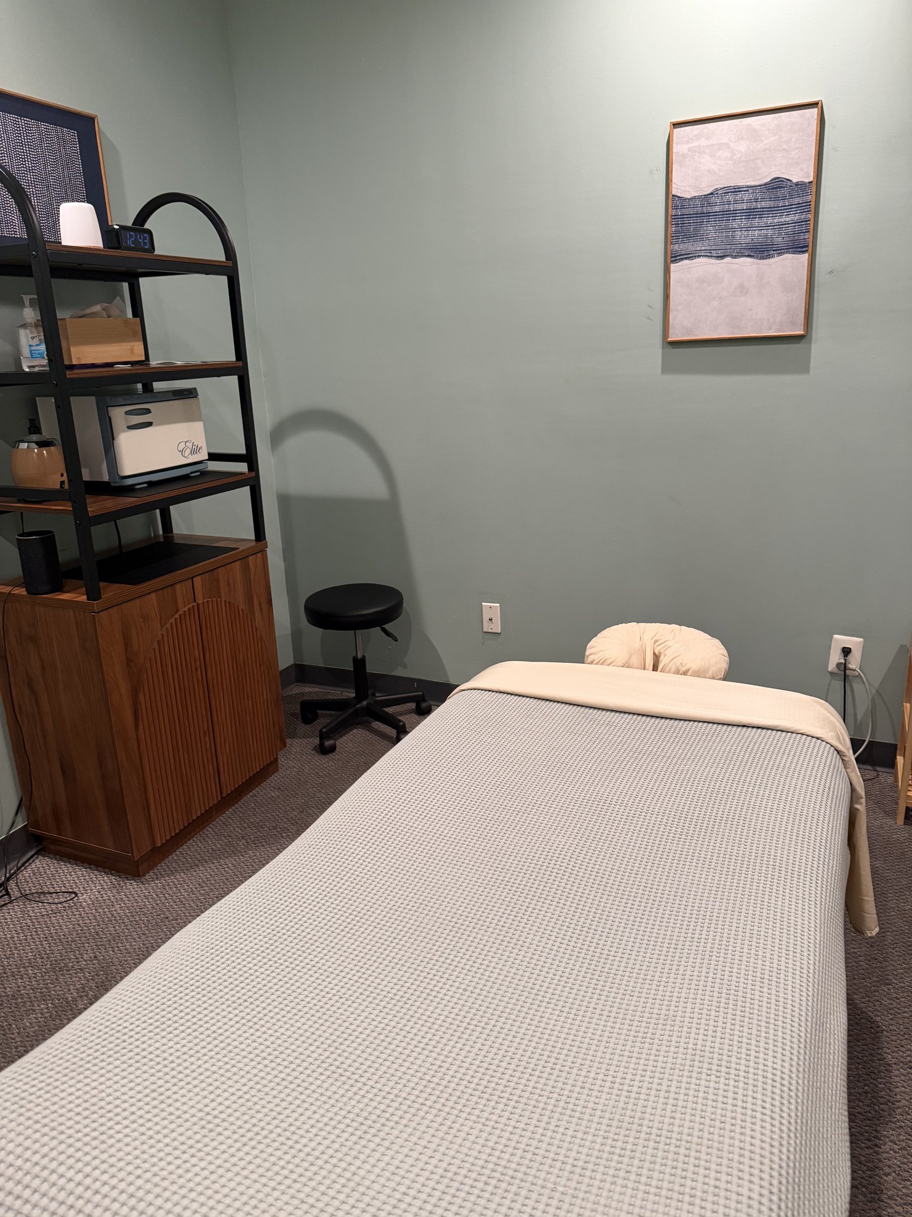 Treatment room with a massage table, stool, and shelving